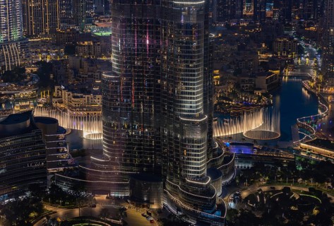 A picture of the Dubai Fountain Show, at night, and the bottom of the Burj Khalifa, next to other