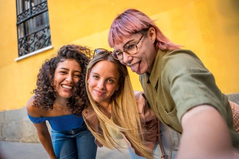 Happy female friends grimacing and sticking tongue out while taking selfie in the street