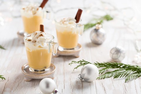 Eggnog with cinnamon and nutmeg for Christmas and winter holidays. With Xmas decorations on wooden