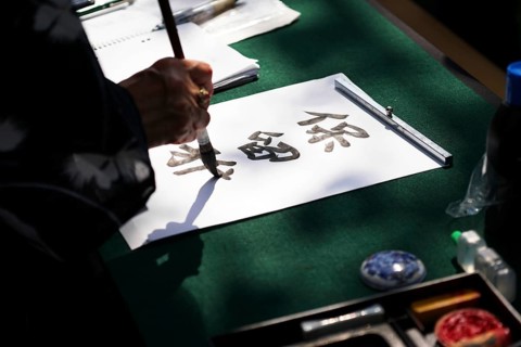 japanese calligraphy, unrecognizable person writing kanji characters with ink brush on paper,