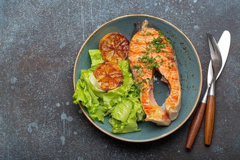 Grilled fish salmon steak and green salad with lemon on ceramic plate on rustic blue stone