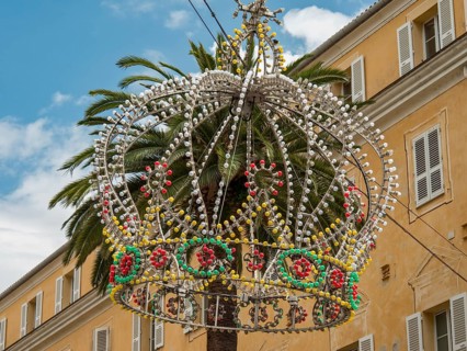 Colourful crown of pearls as decoration on a palm tree in front of a yellow building and blue sky,