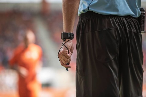 Hand of soccer referee with wristwatch and whistle.