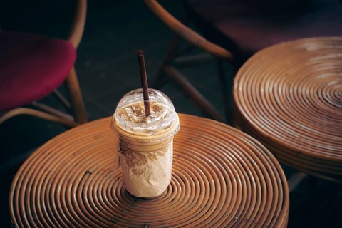 Iced coffee cup on a round rattan table surrounded by wicker chairs, evoking a cozy vibe