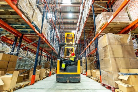 Full length wide photo of a worker using forklift in a storage warehouse
