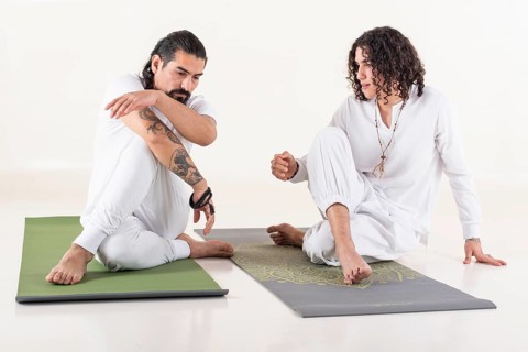 A yoga instructor is teaching yoga to a young man. Both dressed in white yoga clothes. Front view