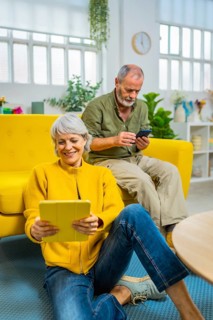 Senior couple using digital tablet and mobile phone spending time relaxed at home