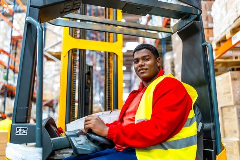 Side view of a happy latin american worker driving forklift in a storage warehouse