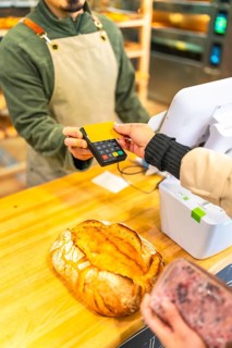 Vertical cropped photo of the hands of a woman paying using credit card in a modern bakery