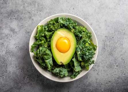 Salad bowl with kale for balanced menu, raw egg yolk in fresh cut half avocado rich in healthy fats