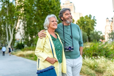Mature caucasian man with a camera and wife visiting an urban park walking together