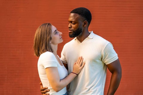 Mixed-raced couple standing embracing and looking at each other against red brick wall