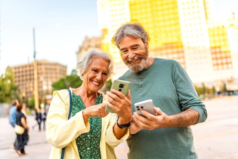 Frontal portrait of a cute modern senior couple having fun using smartphone in the city
