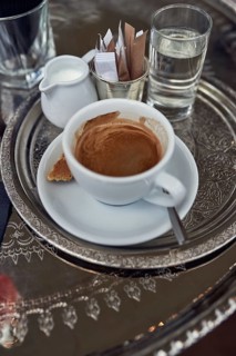Cup of strong espresso coffee with milk on the side in a jug and a glass of water on a tray in a