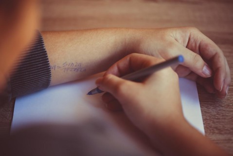 Cropped shot of student using cheat sheet on math exam, reading written formula on hand while