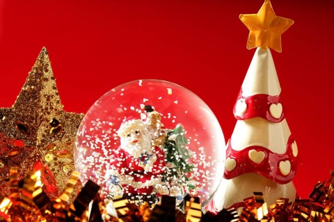 Santa claus figurine on a glass snowing ball, red background studio shot