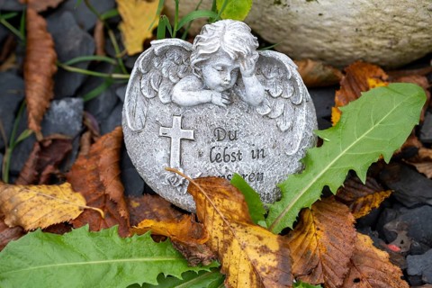 Angel figure on a grave with autumn leaves at the cemetery in Garbsen-Stelingen, Lower Saxony,