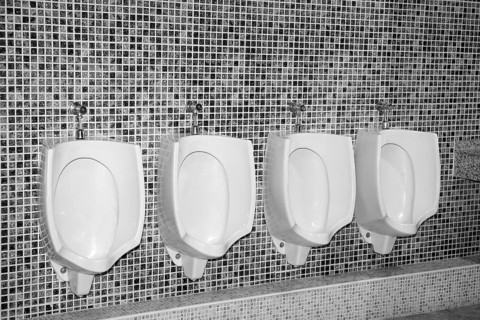 Bathroom urinal in a row with gray tiles black and white
