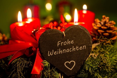 Christmas greetings: Heart with the inscription FROHE WEIHNACHTEN in front of Christmas decorations