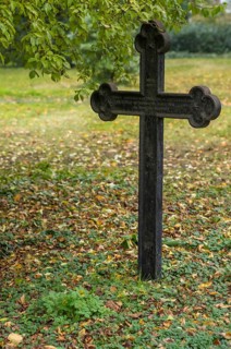 Weathered iron cross marking a grave in a cemetery during the fall season