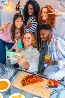 Multi-ethnic friends taking selfie celebrating party eating snacks and drinking in a urban rooftop