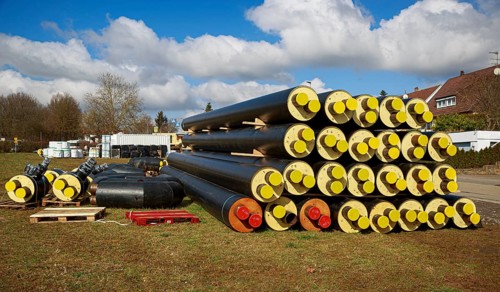 Stacked district heating pipes and district heating lines with yellow ends lie piled up in a meadow
