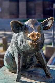 Bronze sculpture of a smiling wild boar in a sitting position, pig bridge with the group of figures