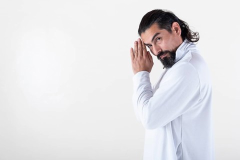 A man dressed in white clasping hands while looking at camera over white background. Tadasana yoga