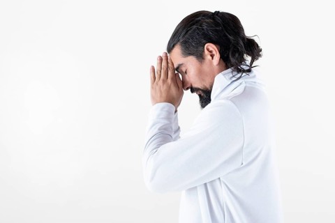 A man dressed in white clasping hands while meditating over white background. Tadasana yoga pose.