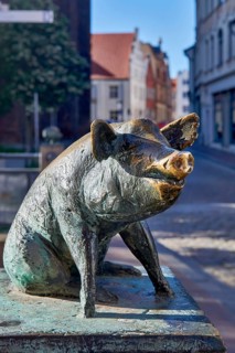 Bronze sculpture of a wild boar on a pedestal in front of a city backdrop, pig bridge with a group