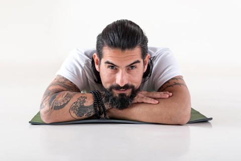 Portrait of a man dressed in white yoga clothes lying on a mat while looking at camera over white