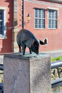 Bronze sculpture of a wild boar on a pedestal in front of a red building, pig bridge with a group