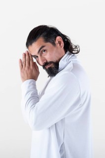 A man dressed in white clasping hands while looking at camera over white background. Tadasana yoga