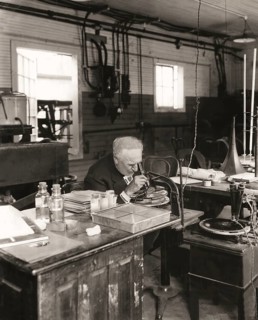 Thomas Alva Edison examining a phonograph disc under a microscope, digitally edited