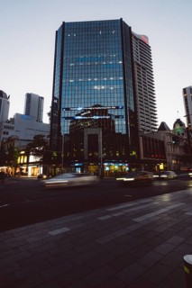 High-rise building with reflective glass façade at dusk, city lights and passing cars, new Zealand