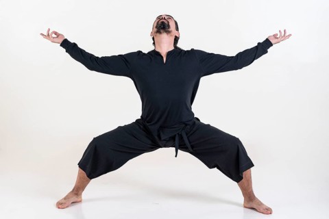 A man dressed in black doing yoga over white background. Utkata konasana yoga pose. Studio shot
