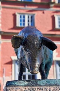 Bronze sculpture of a wild boar in front of a red building with windows, pig bridge with a group of