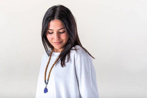 Portrait of a young woman dressed in white yoga clothes over white background wearing a japa mala.