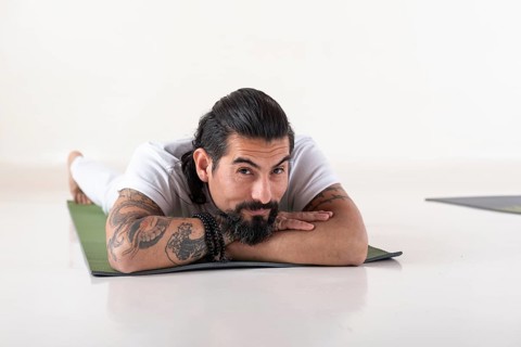Portrait of a young man dressed in white yoga clothes lying on a mat while looking at camera over