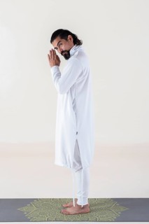 A man dressed in white on a mat, clasping hands while looking at camera over white background.