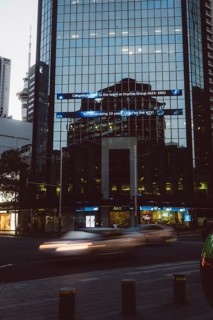Reflective glass facade of a high-rise building in a city at night, light traces from passing cars,