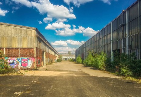 Industrial site with graffiti and sprawling vegetation under a blue sky, Gerresheimer Germany, Lost