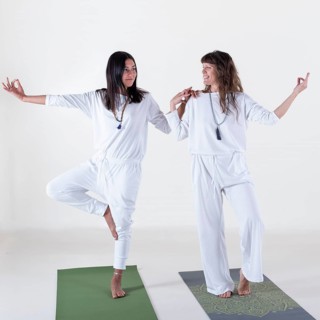 Two women dressed in white doing yoga over white background. One is teaching the other. Studio shot