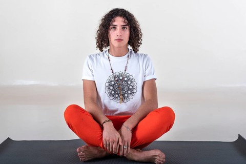 Man sitting cross-legged on a mat about to meditate while looking at camera over white background.