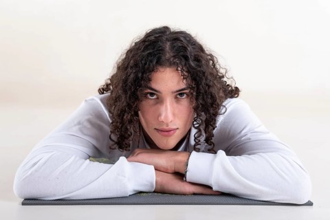 Portrait of a young man dressed in white yoga clothes lying on a mat while looking at camera over