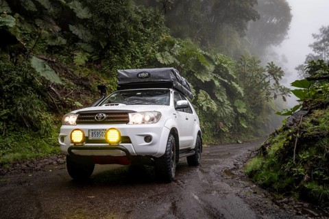 Off-road vehicle in the fog in the rain, with fog lights on a narrow road, dense vegetation on a