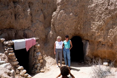 Two tourists standing in front of the entrance to cave dwellings, Matmata, Tunisia, North Africa,