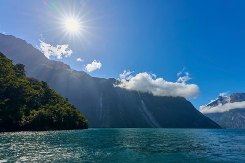 Clear sun over a fjord, surrounded by majestic mountains and a slightly cloudy sky, summer, Milford