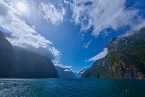 Sunlit mountains surrounded by deep water and clouds, summer, Milford Sound, Te Anau, Fiordland
