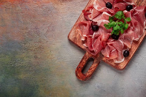 Sliced prosciutto, on a cutting board, with olives and herbs, snack, breakfast, no people